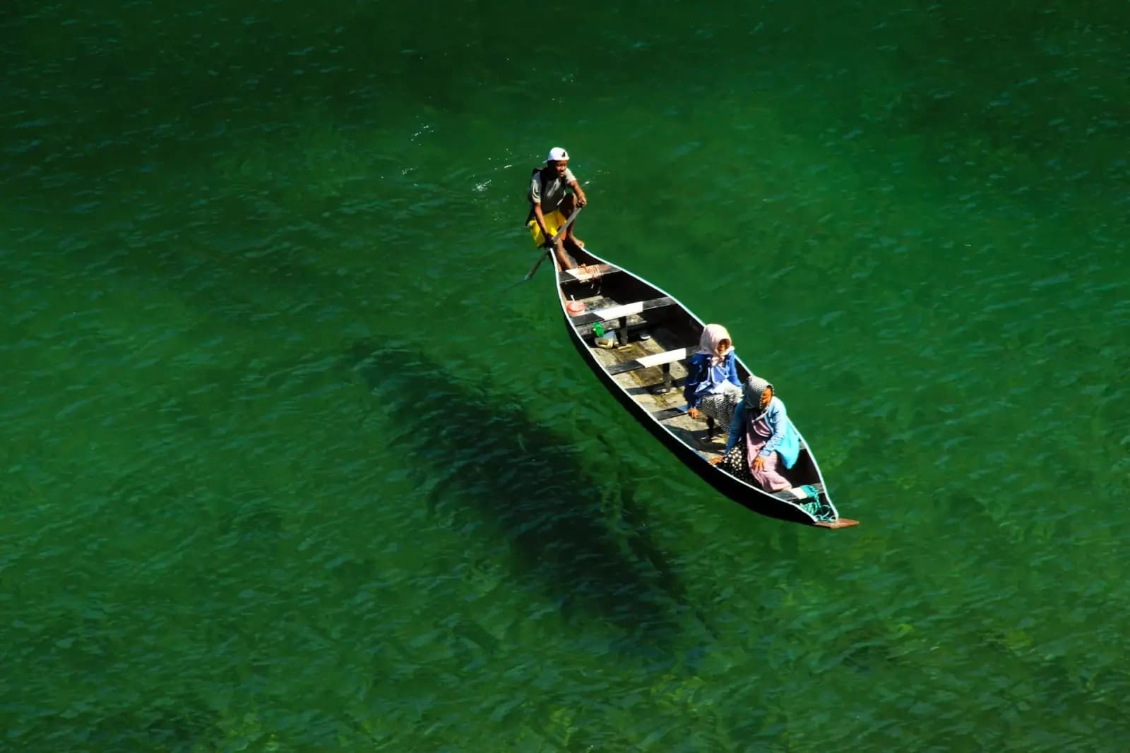 Boatman rowing a wooden boat across green water on a Tentasy expedition